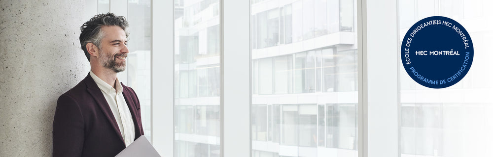 Personne dans un espace de bureaux moderne devant une baie vitrée, avec le sceau HEC Montréal en français visible.