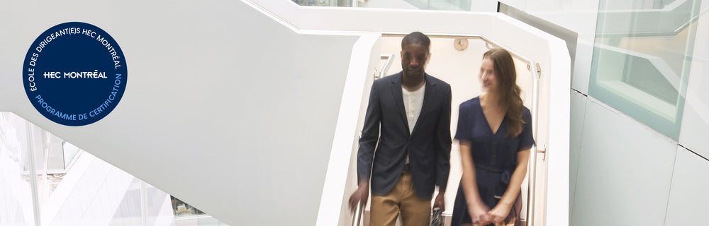 Deux personnes circulant dans un atrium moderne et lumineux, avec le sceau HEC Montréal en français visible.